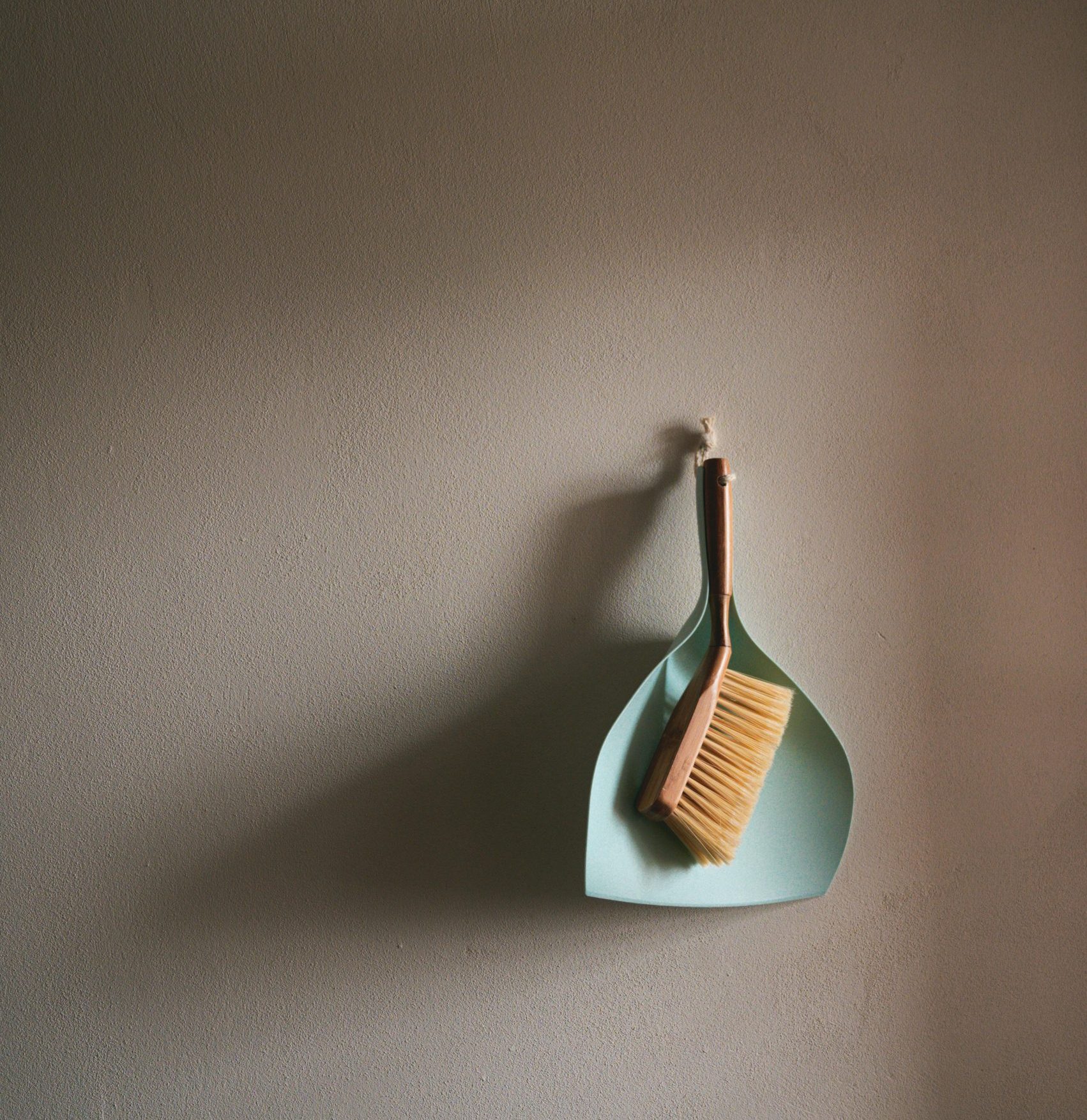 Dustpan and brush hanging on a wall, ready to sweep loose debris during a garden tidy-up