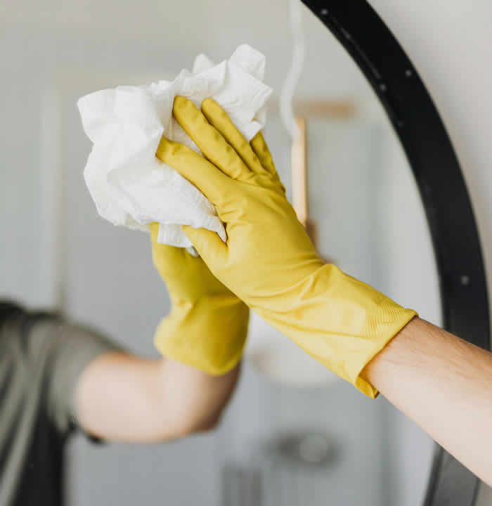 Gloved hand wiping a mirror to remove surface marks and restore clear glass